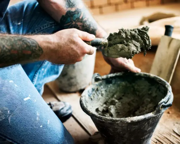 Murarz z tatuażami nabiera zaprawę murarską z plastyfikatorem na kielnię. Proporcje są kluczowe dla trwałości budowli.