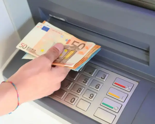 Dłoń trzyma banknoty 50 euro przy bankomacie. W Hiszpanii, jak w całej strefie euro, obowiązuje euro.
