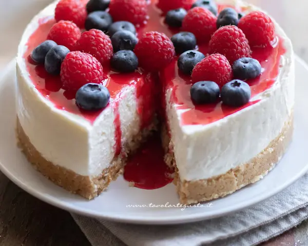 Delizioso cheesecake con mascarpone, guarnito con lamponi freschi, mirtilli e una cascata di salsa rossa.