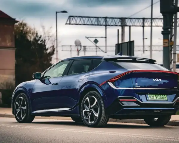 Granatowe Kia EV6 GT z charakterystycznym pasem świateł z tyłu, zaparkowane przy drodze z widoczną infrastrukturą kolejową.