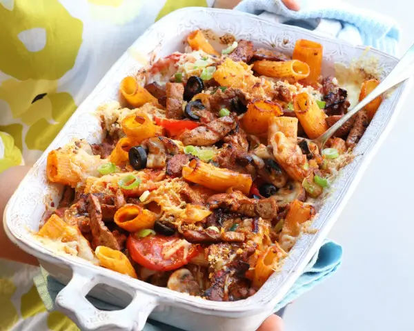 Pyszna zapiekanka gyros z makaronem, podana w białym naczyniu, z widocznymi kawałkami mięsa, oliwek i pomidorów.