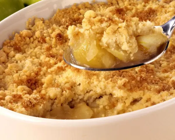 Une cuillère de crumble aux pommes, parfait pour suivre la recette Cyril Lignac. Des pommes fondantes sous une pâte croustillante.