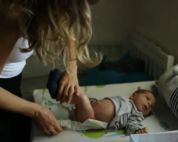 Mama zmienia pieluszkę noworodkowi. Zastanawiasz się, ile kupić pieluszek dla noworodka? Warto mieć zapas!