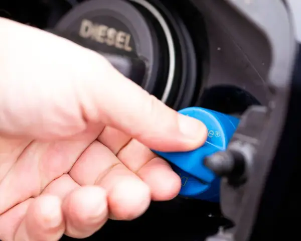 Hand schraubt blauen AdBlue-Deckel auf Diesel-Tanköffnung. AdBlue ist eine Harnstofflösung zur Abgasreinigung bei Dieselfahrzeugen.