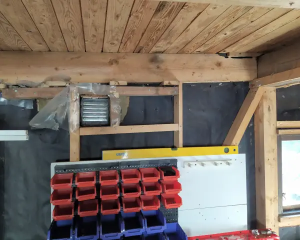 Pågår arbete för att isolera garage. Syns träbjälkar, isolering och förvaringssystem med fack.