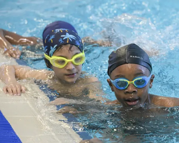 Deux enfants avec des bonnets et lunettes de natation dans une piscine.