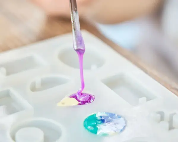 A person is learning how to make an epoxy resin mold by carefully pouring colored resin into a silicone mold.