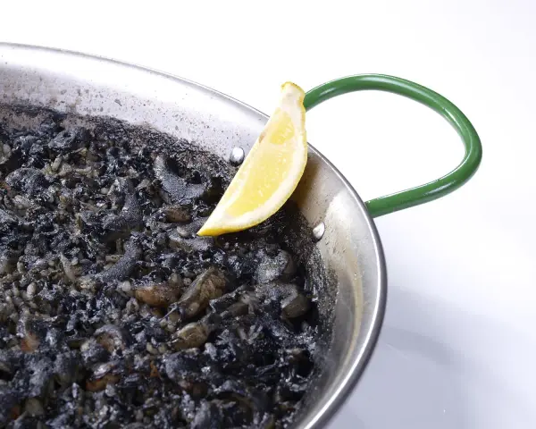 Arroz negro en paellera, con trozos de calamar y un gajo de limón.