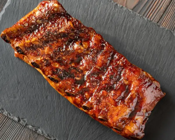 Costillas a la miel, glaseadas y jugosas, servidas sobre una pizarra oscura.