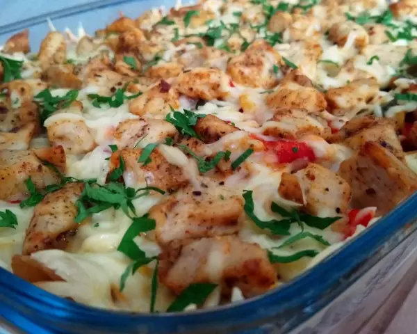 Pyszna zapiekanka gyros z makaronem, posypana serem i natką pietruszki, w szklanym naczyniu.