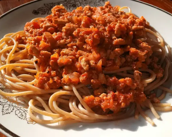 Porcja pysznego spaghetti bolognese z aromatycznym sosem mięsnym i pomidorowym, podana na talerzu z ozdobnym wzorem.