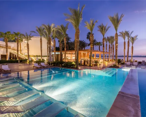 Luxury resort pool with palm trees and lounge chairs at dusk.