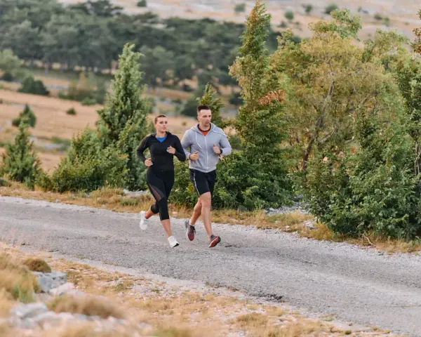 Coppia corre su strada sterrata, immersa nel verde. Il loro passo è un fondo lento, godendosi la natura.