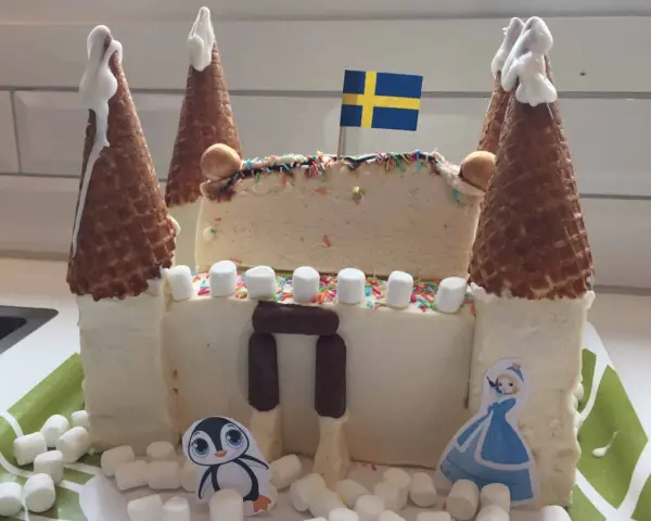 En fantasifull glasstårta slott med svenska flaggan, marshmallows och en söt pingvin.