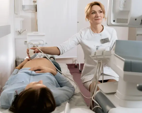 Lekarka wykonuje badania prenatalne, pokazując przyszłej mamie, jak się przygotować do wizyty.