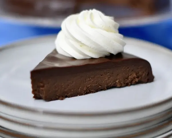 En bit fransk chokladtårta med en virvel av vispad grädde på en tallrik.