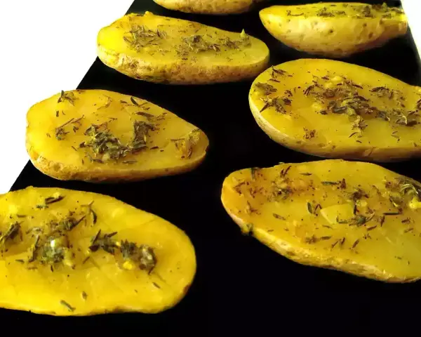 Patatas al microondas cortadas por la mitad, sazonadas con hierbas y especias, listas para cocinar.