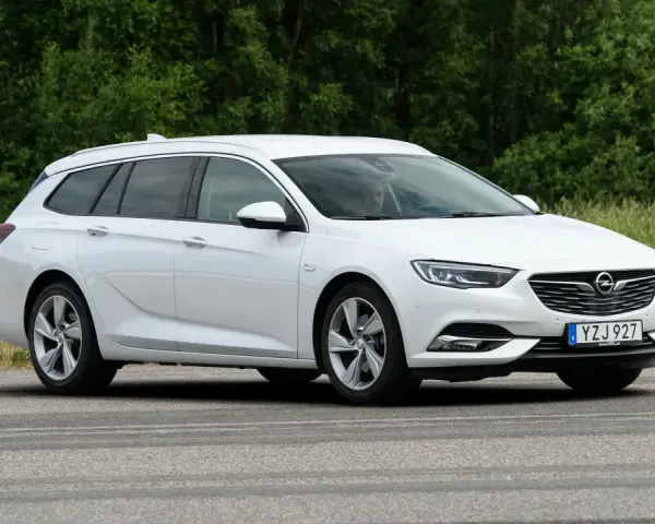 Vit Opel Insignia kombi parkerad vid en grönskande skog. En förare syns i bilen, kanske funderar på ett opel insignia problem.