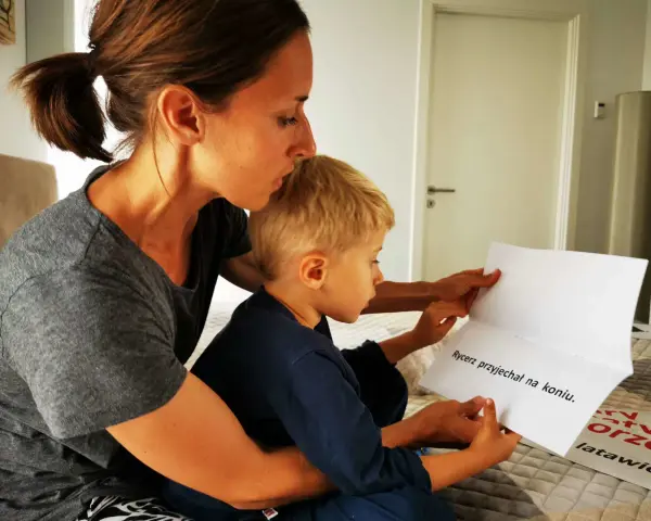 Mama pomaga synkowi, jak nauczyć się czytać, wskazując palcem na tekst "Rycerz przyjechał na koniu".