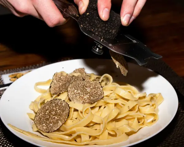 Dłonie trą całe grzyby trufle nad talerzem tagliatelle.