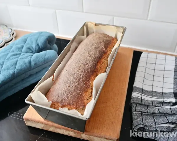 Świeżo upieczony chleb cebulowy na zakwasie w keksówce, gotowy do wyjęcia. Obok rękawica kuchenna i ściereczka.