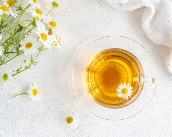 Un mazzolino di margherite e una tazza di tisana dorata. Nonostante la sua apparenza innocua, la camomilla fa male al cuore se consumata in eccesso.