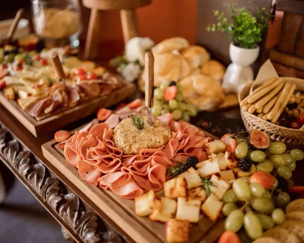 Stół z przekąskami: wędliny, sery, owoce, pieczywo i paluszki.