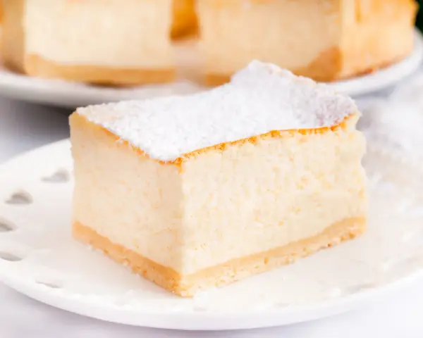Puszysty sernik z mascarpone, oprószony cukrem pudrem, na białym talerzyku. Idealny na deser.