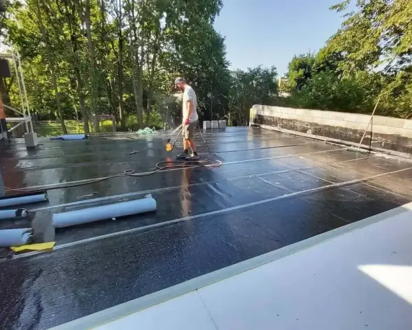 Pracownik wykonuje hydroizolację tarasu nad garażem, używając palnika do zgrzewania papy.