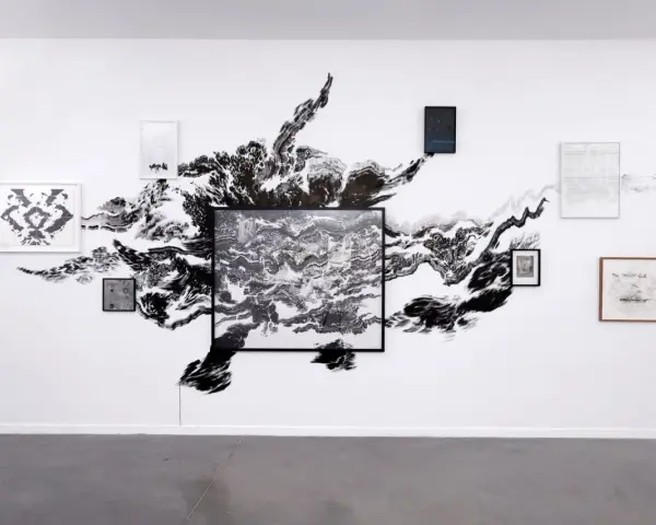 Œuvres d'Abdelkader Benchamma : une explosion d'encre noire sur mur blanc, encadrée par des dessins et peintures.