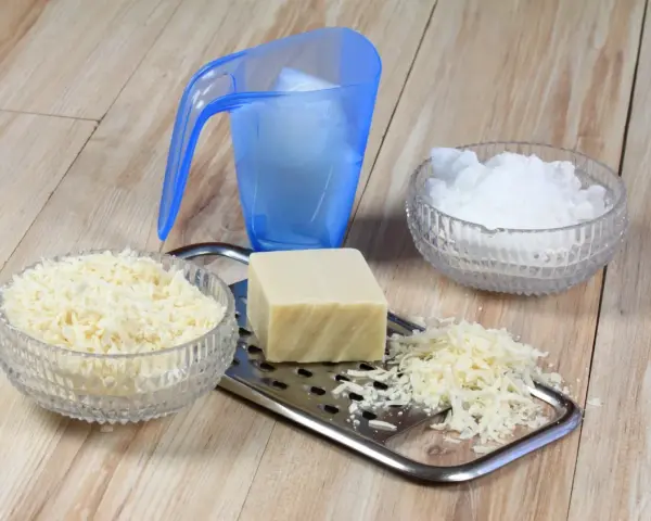 Ingrédients pour une lessive maison : savon râpé, cristaux de soude et un bloc de savon sur une râpe.