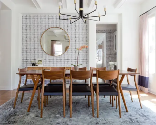 Tavolo da pranzo in legno con sedie in pelle nera, tappeto sotto il tavolo da pranzo si, con carta da parati a motivi geometrici e specchio rotondo.