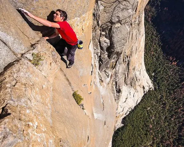 Ein Mann klettert free solo eine steile Felswand empor, mit einem tiefen Abgrund unter ihm.