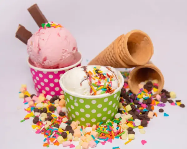 Zwei Becher mit Eiscreme, einer rosa, der andere weiß, bestreut mit bunten Streuseln und Schokostückchen. So sieht leckeres Gelato aus!