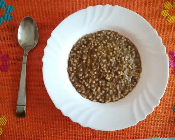 Piatto di pasta e lenticchie fumante, pronto per essere gustato. Un cucchiaio d'argento attende accanto.