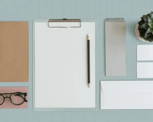 Un exemple de book artistique : un carnet brun, des lunettes, un presse-papiers avec un crayon, un carnet gris, une plante verte, des cartes de visite et une enveloppe.