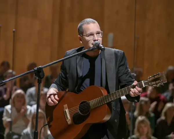 Artysta w okularach gra na gitarze podczas koncertu Męskie Granie. Publiczność w tle.