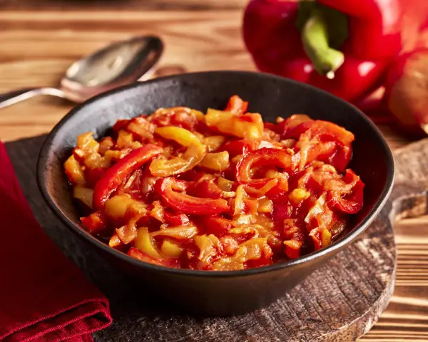 Schmor paprika mit Zwiebeln, ein Gericht, das man gut letscho selber machen kann. Serviert in einer Schüssel auf einem Holztisch.