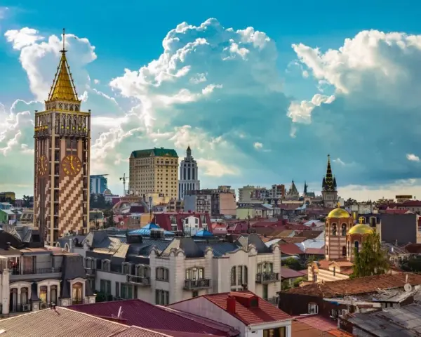 Widok na stolicę Adżarii, Batumi, z charakterystyczną wieżą zegarową i złotymi kopułami cerkwi pod błękitnym, chmurowym niebem.