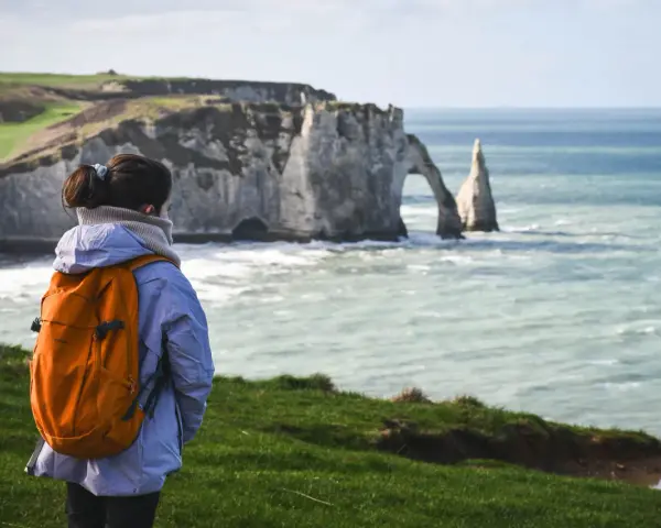 Une randonneuse admire les falaises d'Étretat, un paysage spectaculaire rappelant la beauté sauvage de la baie de Somme.