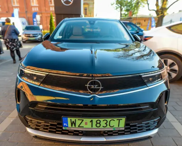 Czarny Opel z zieloną tablicą rejestracyjną WZ 183CT na tle innych samochodów.