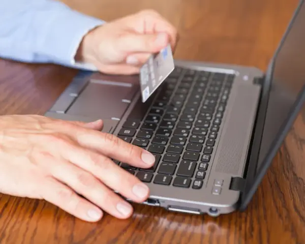 Mężczyzna z kartą płatniczą przy laptopie, szuka informacji jak sprawdzić blokady na koncie PeoPay.