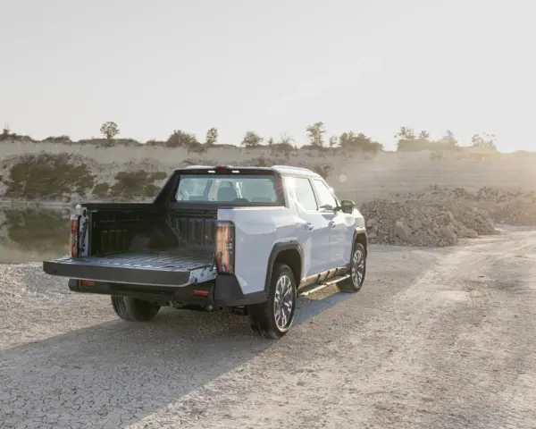 Biały maxus pickup z otwartą paką stoi na żwirowej drodze przy zbiorniku wodnym.
