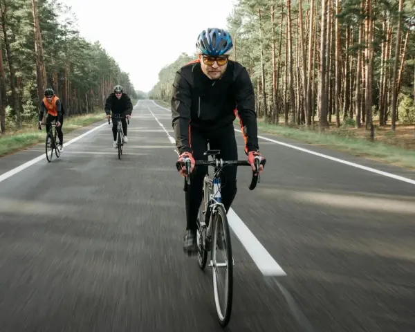 Cyclists on a road through a forest, likely engaged in a VO2 max training program, pushing their limits.