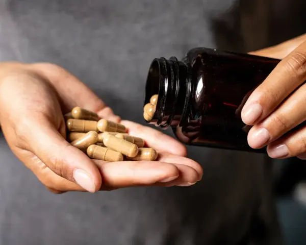 Hände schütten Kapseln aus einer braunen Flasche. Die Kapseln liegen in der Handfläche, bereit zur Einnahme. Möglicherweise zur Unterstützung der chrom wirkung.