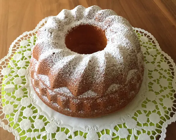 Ein goldbrauner Quark Gugelhupf, bestäubt mit Puderzucker, auf einer zarten Spitzendeckchen.