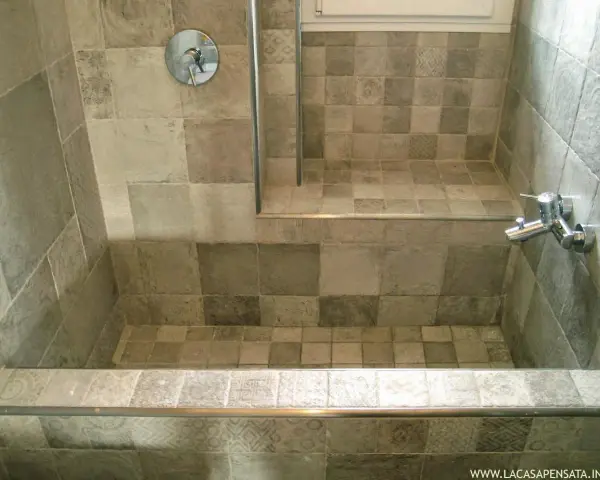 Bagno con vasca da bagno in muratura fai da te, rivestita con piastrelle grigie di varie tonalità e fantasie.