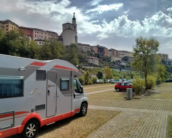 Camper in sosta a Belluno, con case colorate e un campanile sullo sfondo.
