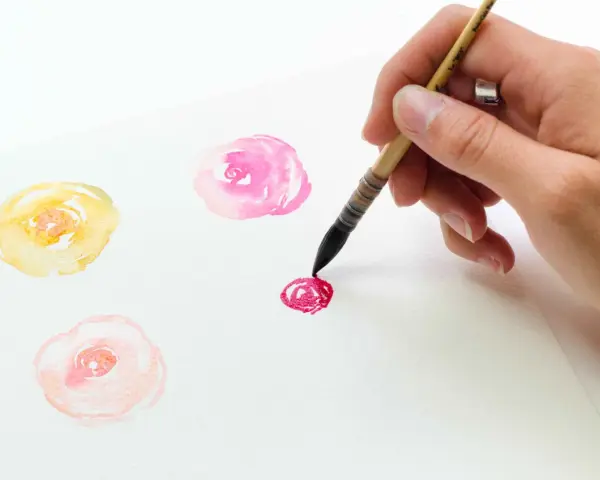 Un dessin de champs de fleurs facile à l'aquarelle. Une main peint des roses délicates en jaune, rose et rouge sur du papier blanc.