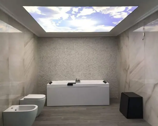 Bagno moderno con vasca, bidet e WC. Il soffitto in cartongesso riproduce un cielo azzurro con nuvole, creando un'atmosfera rilassante.